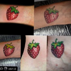 Фото тату маленькой, реалистичной клубники с зелеными листьями на женском запястье. Яркий рисунок татуировки, выполненный в красных и зеленых тонах.