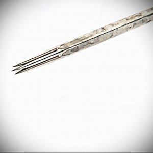 Макросъемка тату-иглы с несколькими острыми кончиками. Игла выглядит стерильной и готовой к использованию, демонстрируя детали ее конструкции.