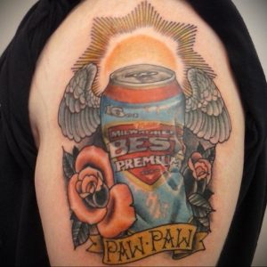 Фото тату на плече с изображением банки пива Pabst Blue Ribbon, окруженной крыльями и розой. Яркий и стильный эскиз.