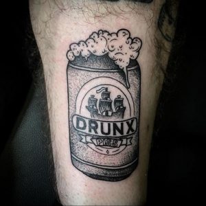Фото тату на ноге с изображением банки пива "Drunk Piss" с изображением корабля. Черно-белый эскиз в минималистичном стиле.