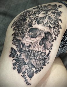 Фото тату на бедре: череп, увитый розами и грибами, выполнен в технике black and grey с высокой детализацией.