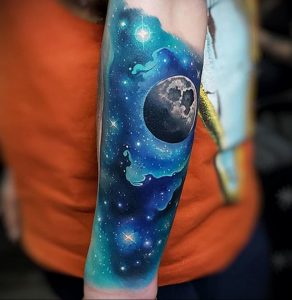 Фото тату: реалистичное изображение космоса с луной и звездами, выполненное на руке. Детализированный рисунок с использованием синих и фиолетовых оттенков.
