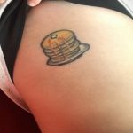 Небольшая цветная татуировка на бедре с изображением стопки блинчиков, политых кленовым сиропом. Аппетитный и милый рисунок.
