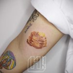 Фото тату на руке, изображающее стопку блинов с надписью "MAKE YOU". Простой и стильный рисунок татуировки.