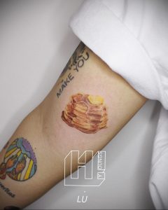 Фото тату на руке, изображающее стопку блинов с надписью "MAKE YOU". Простой и стильный рисунок татуировки.