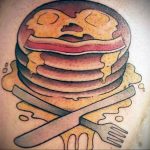 Фото тату стопки блинчиков с беконом, яйцами и приборами на руке. Оригинальный рисунок татуировки в стиле олдскул с детальной проработкой.