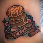 Фото тату блинчиков с надписью "Stack 'em high!" и ягодами на руке. Яркий рисунок татуировки в стиле олдскул с детальной проработкой.