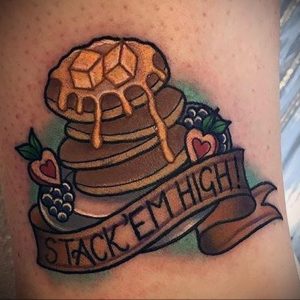 Фото тату блинчиков с надписью "Stack 'em high!" и ягодами на руке. Яркий рисунок татуировки в стиле олдскул с детальной проработкой.