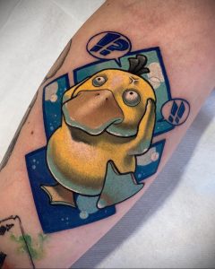 Фото тату Psyduck на предплечье. Желтый покемон Psyduck с вопросительным знаком над головой. Яркий и красочный рисунок татуировки в стиле аниме.