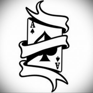 Фото тату: стилизованное изображение карты Ace of Spades с лентой, обернутой вокруг нее, выполненное в черном цвете.