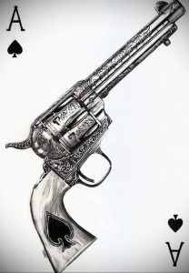 Фото тату: детально прорисованный револьвер на фоне карты Ace of Spades, выполненный в черно-белой гамме.