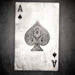 Фото тату с изображением туза пик в винтажном стиле на фоне текстурированной поверхности.