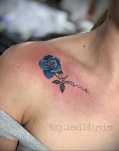 Фото тату голубой розы на плече с надписью 'Amilia'. Изящный рисунок татуировки выполнен в мягких тонах.