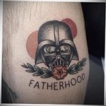 Фото тату Дарта Вейдера с надписью "Fatherhood" на руке, выполненное в традиционном стиле с использованием черных линий и простых цветов.
