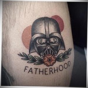 Фото тату Дарта Вейдера с надписью "Fatherhood" на руке, выполненное в традиционном стиле с использованием черных линий и простых цветов.