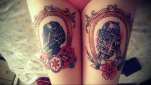 Фото тату на бедрах с изображением Дарта Вейдера и дроида R2-D2 в старинных рамках, украшенных цветами и символикой 'Звездных войн'.