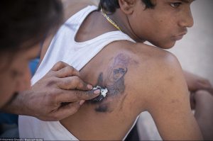 Фотография процесса нанесения татуировки на плечо, мастер наносит рисунок, клиент держит салфетку.