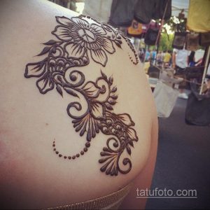 Фотография рисунка хной на плече, выполненного в традиционном восточном стиле. Рисунок состоит из цветов и растительных орнаментов, выполненных коричневой хной.