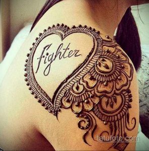 Фото тату хной на плече с надписью 'Fighter' внутри сердца, восточный орнамент, коричневые тона, символ борьбы и стойкости.