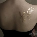 Фото тату с изображением золотой ветви с листьями, изящно изогнутой вдоль спины. Нежный и элегантный рисунок, выполненный в минималистичном стиле.