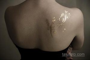 Фото тату с изображением золотой ветви с листьями, изящно изогнутой вдоль спины. Нежный и элегантный рисунок, выполненный в минималистичном стиле.