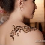 Фото тату: детализированный рисунок дракона и цветка сакуры на женской лопатке. Черно-белая графика с высокой детализацией.