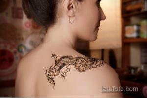 Фото тату: детализированный рисунок дракона и цветка сакуры на женской лопатке. Черно-белая графика с высокой детализацией.