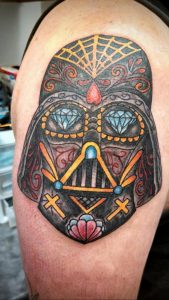 Фото тату Дарта Вейдера, стилизованного под Sugar Skull, на плече. Цветная татуировка с использованием ярких оттенков и сложных узоров.
