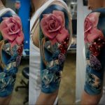 Фото татуировки розы и подковы на руке. Яркий и красочный рисунок татуировки выполнен в стиле реализм с использованием розовых, синих и золотых оттенков.