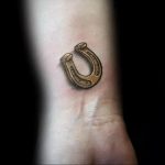 Фотография минималистичной татуировки подковы на запястье. Простой, но стильный рисунок татуировки выполнен в коричневых тонах.