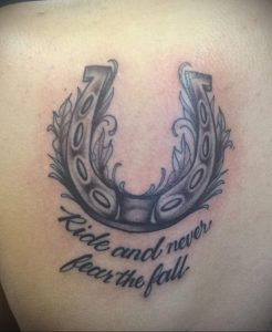 Фото тату подковы с крыльями и надписью 'Ride and never fear the fall' на боку. Мотивационный рисунок татуировки в стиле графика.