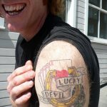Фото тату: татуировка с изображением игральных карт, подковы и надписи 'Lucky Devil' на плече.