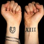 Фото тату: две татуировки на запястьях - подкова и римские цифры XIII, выполненные черными чернилами.