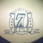 Фото тату цифры 7 с именем EMF на ленте. Простой рисунок татуировки в стиле олдскул с использованием черного цвета.