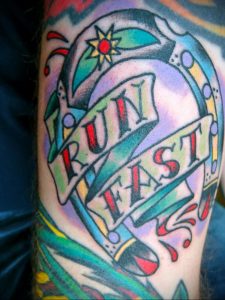 Фото тату на руке: подкова с надписью 'RUN FAST', выполненная в ярких и насыщенных цветах. Динамичный и мотивирующий рисунок татуировки.