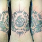 Фото тату подковы, внутри которой пачки денег. Рисунок выполнен в черно-серых тонах с добавлением красных акцентов. Расположение на предплечье.