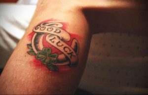 Фото тату подковы, четырехлистного клевера и надписи 'Good Luck' на руке, выполненное в ярком и красочном стиле.