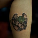 Фото тату подковы с инициалами 'G.M.A.M' на ленте, выполненное в реалистичном стиле с использованием мягких оттенков.