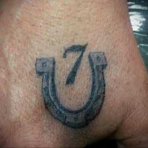 Фото тату подковы с цифрой 7 внутри. Минималистичный черно-белый рисунок татуировки на руке.