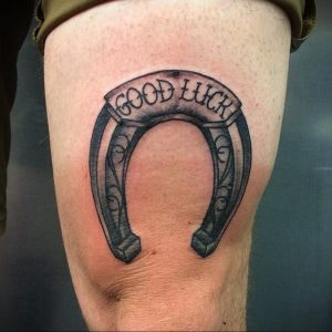 Фото тату подковы с надписью 'GOOD LUCK' на ноге. Черно-серая татуировка в минималистичном стиле с четкими линиями.