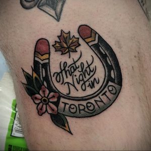 Фото татуировки в стиле олд скул с изображением подковы, надписи "That Night in Toronto", кленового листа и цветка. Яркие цвета, четкие контуры.