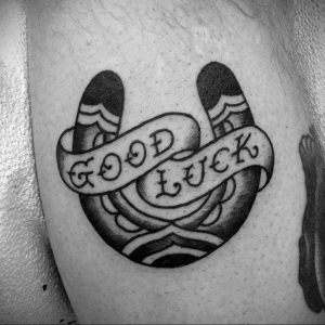 Фото татуировки подковы в стиле олд скул с надписью "Good Luck" на ленте. Яркие цвета, четкие контуры, традиционный стиль.