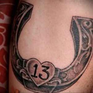 Фото тату на руке: подкова с числом 13 внутри, выполненная в стиле blackwork. Черно-белая татуировка, детализированный рисунок.