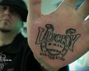 Фото тату надписи 'Lucky Bail Bonds' на руке. Черно-белый рисунок татуировки с изображением двух кубков.