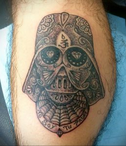 Фото татуировки в стиле Sugar Skull с изображением черепа Дарта Вейдера. Череп украшен яркими узорами и цветами, а в глазницах расположены бриллианты.