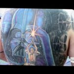 Большая татуировка на спине с изображением Дарта Вейдера, сражающегося на фоне космической битвы с участием истребителей TIE Fighter и X-Wing. Детализированный рисунок татуировки.