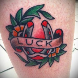 Фото тату подковы с надписью 'LUCK' в стиле традиционной татуировки на ноге. Простой, но эффектный рисунок татуировки с использованием ярких цветов.
