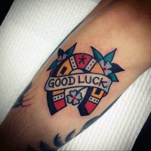 Фото тату подковы с клевером и надписью 'Good Luck' в стиле олд скул на руке. Яркие цвета, четкие контуры, символы удачи.