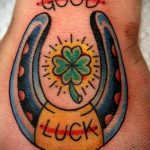 Фото тату на запястье: подкова, клевер и надпись 'Good Luck' в стиле олд скул с яркими цветами и четкими линиями.