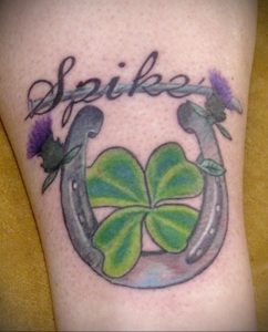 Фото тату на руке с изображением двух подков, клевера и надписи 'Spike' в черно-серых тонах.